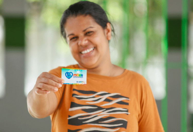 Mulher sorrindo e segurando cartão do Mães de Pernambuco.