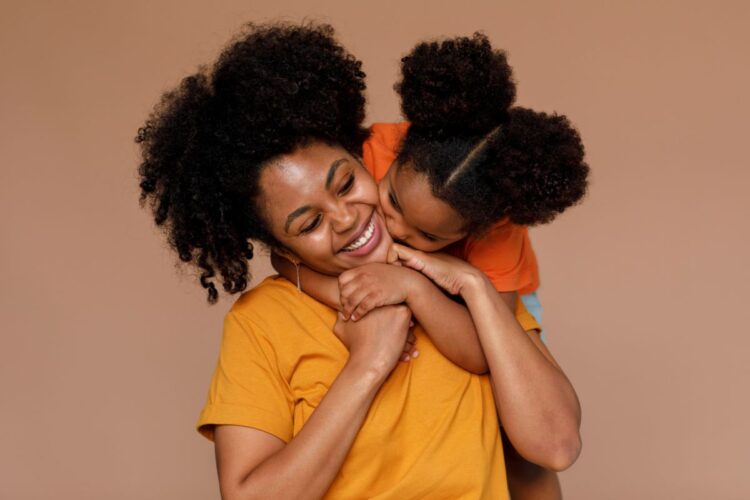 Mãe sorrindo enquanto recebe um abraço carinhoso da filha pequena