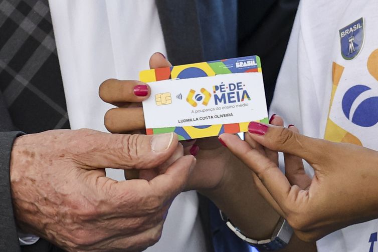 Cartão do Programa Social Pé de Meia, voltado para estudantes do ensino médio público, sendo entregue a uma estudante.
