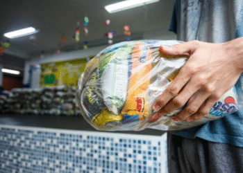 Pessoa segurando saco plástico com cestas básicas do programa Cesta da Família