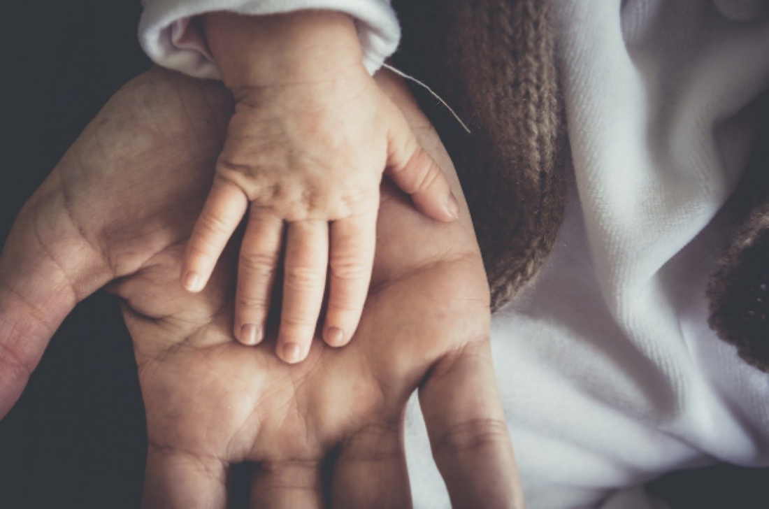 Mão de pai segurando a mão de um bebê, simbolizando o apoio e cuidado na paternidade.