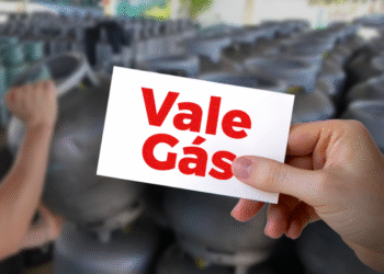 Cartão do Novo Vale Gás com o texto 'Vale Gás' sendo segurado por uma mão, com fundo de cilindros de gás