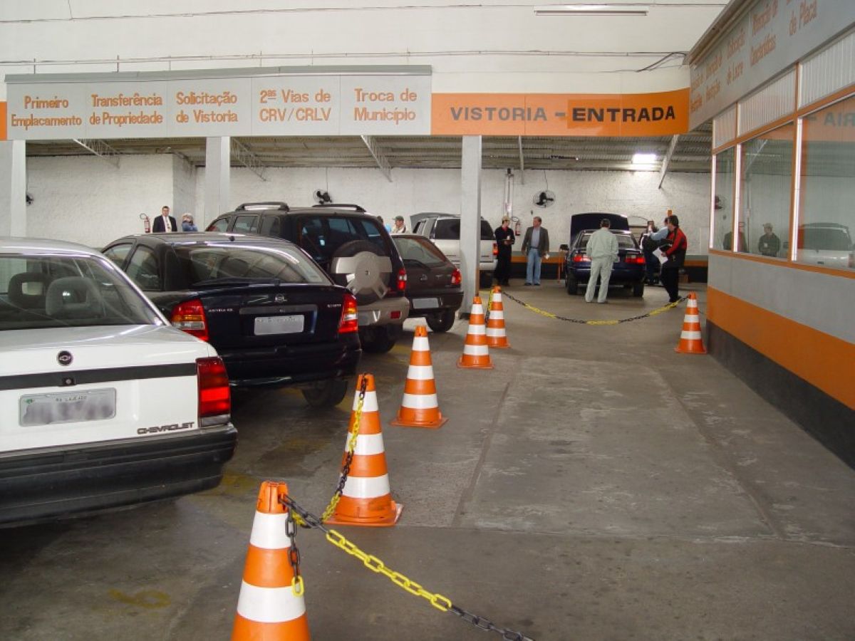 Pátio de vistoria com veículos em fila e atendentes analisando documentos e automóveis.