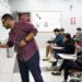 Professor escrevendo no quadro durante aula em sala com estudantes atentos.