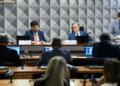 Membros da Comissão Mista do Congresso Nacional, reunidos em sessão de votação, com notebooks abertos e documentos sobre a mesa.