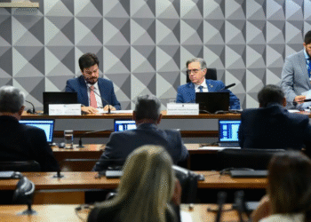 Membros da Comissão Mista do Congresso Nacional, reunidos em sessão de votação, com notebooks abertos e documentos sobre a mesa.