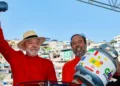 O presidente Luiz Inácio Lula da Silva e o Ministro de Minas e Energia Alexandre Silveira sorriem no palco em Belo Horizonte, segurando um botijão de gás e uma panela de pressão, respectivamente, durante o lançamento do programa Gás do Povo.
