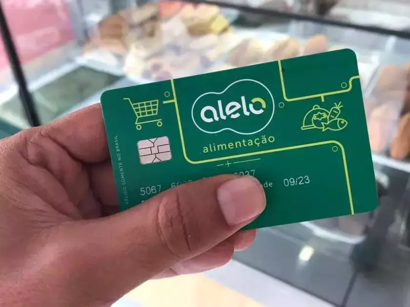 Cartão Alelo Alimentação sendo segurado por uma pessoa, destacando a bandeira do vale-alimentação.