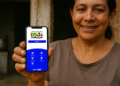 Mulher sorridente segura celular com aplicativo do Bolsa Família aberto.