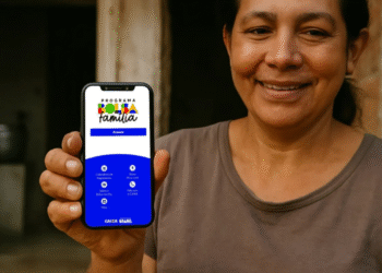 Mulher sorridente segura celular com aplicativo do Bolsa Família aberto.