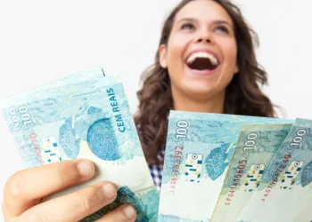Mulher jovem e feliz segurando várias notas de cem reais, simbolizando a alegria de conseguir dinheiro rápido.
