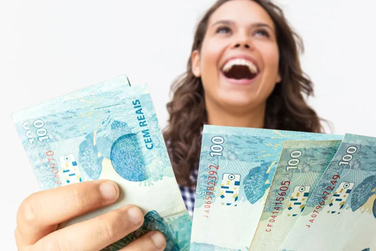 Mulher jovem e feliz segurando várias notas de cem reais, simbolizando a alegria de conseguir dinheiro rápido.