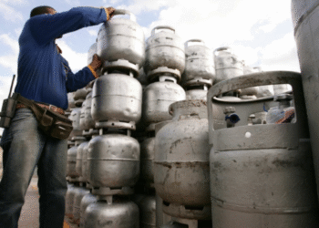 Trabalhador organizando cilindros de gás em depósito com comunicado do Governo sobre o novo Vale Gás.