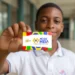 Jovem mostrando o cartão Pé-de-Meia, com a logo e cores vibrantes, representando a poupança do ensino médio.