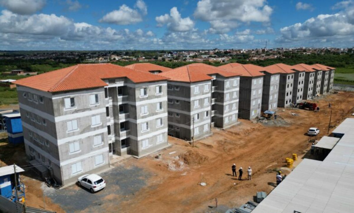 Conjunto habitacional em construção do programa Minha Casa Minha Vida sob céu azul com nuvens.