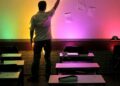 Professor em sala de aula com parede iluminada por luzes coloridas