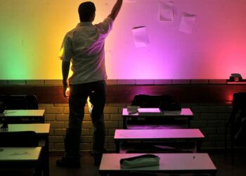 Professor em sala de aula com parede iluminada por luzes coloridas