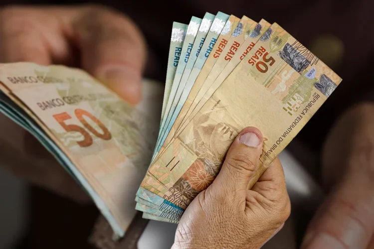 Dinheiro do benefício do BPC de setembro sendo segurado por mãos, representando o pagamento do programa.