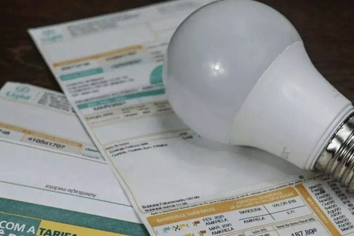 Lâmpada de LED e contas de luz sobre uma mesa, simbolizando o impacto da mudança de bandeira tarifária para o consumidor.