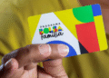 Pessoa segurando o novo cartão do Bolsa Família sobre fundo amarelo.
