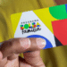 Pessoa segurando o novo cartão do Bolsa Família sobre fundo amarelo.