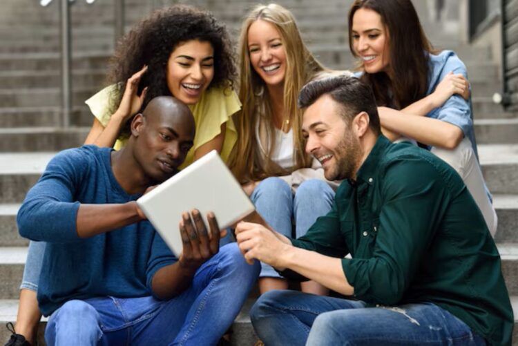Grupo de jovens estudantes diversos e sorrindo, interagindo com um tablet em um ambiente urbano.
