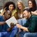 Grupo de jovens estudantes diversos e sorrindo, interagindo com um tablet em um ambiente urbano.