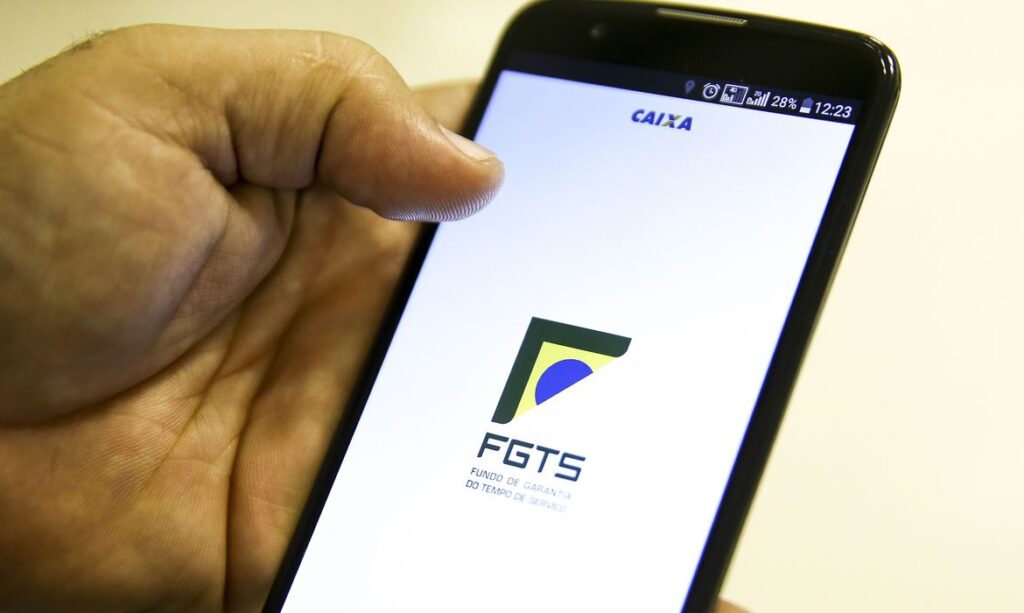 ela de um smartphone mostrando o aplicativo oficial do Fundo de Garantia do Tempo de Serviço (FGTS), com o logo do órgão em destaque. A imagem foca na interface digital que permite aos trabalhadores gerenciar o saldo e as modalidades de saque.