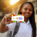Pé de Meia 2025: jovem segurando cartão colorido com texto "Pé de Meia" em fundo de escola ao pôr do sol