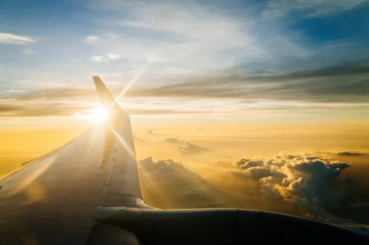 Vista aérea de uma asa de avião ao pôr do sol, com céu dourado e nuvens iluminadas, representando a acessibilidade das passagens aéreas de R$ 200