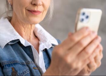 Mulher sênior sorrindo enquanto usa o celular, representando a facilidade da Prova de Vida digital para aposentados.