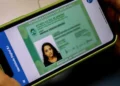 Uma pessoa segura um smartphone que exibe a Carteira de Identidade Digital do Detran-RJ, destacando o documento eletrônico na tela.