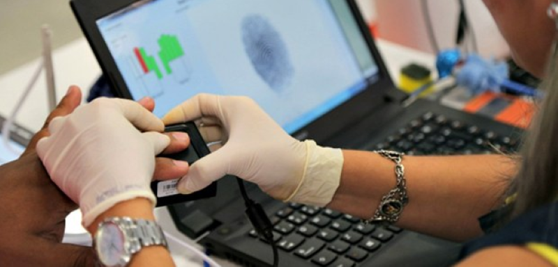 Cadastro biométrico do eleitor com nova regra sendo realizado por pessoa com luvas em um laptop.