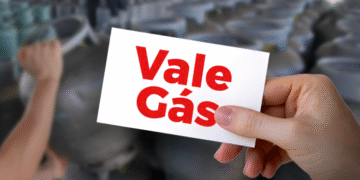 Cartão do Vale-Gás segurado por uma mão com botijões ao fundo