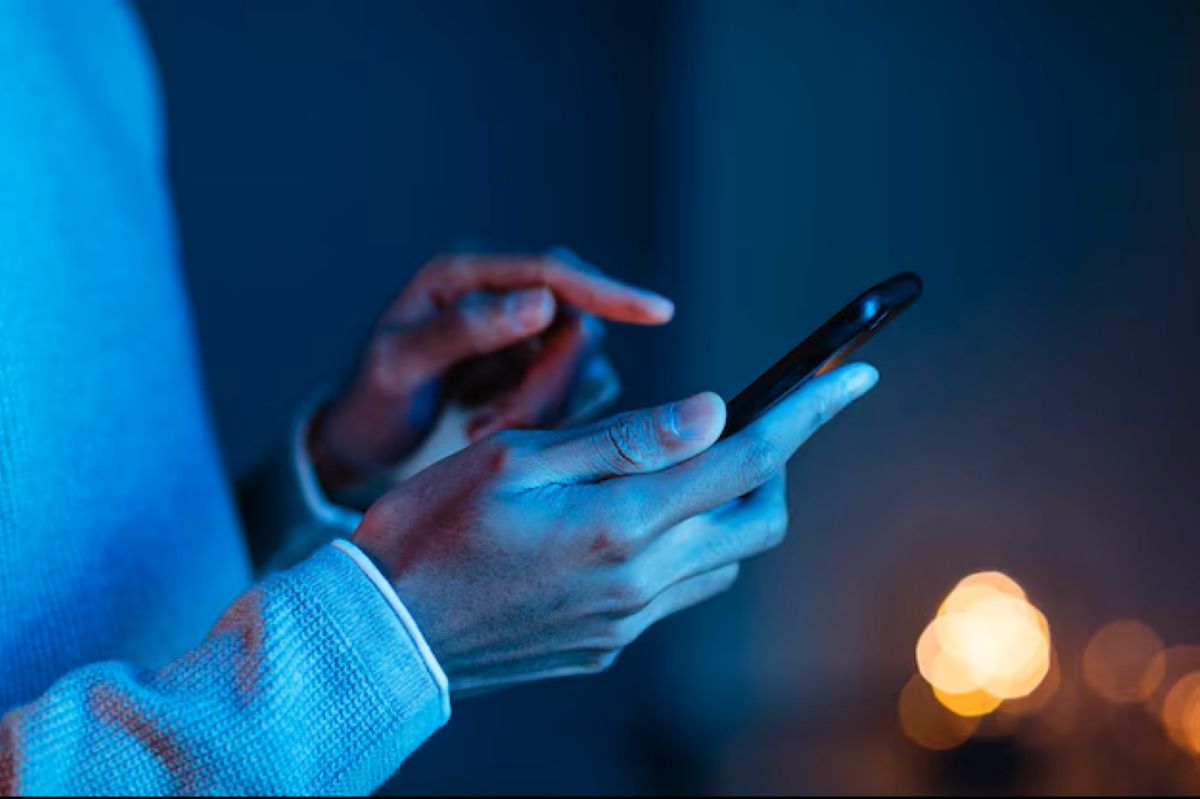 Mãos segurando smartphone em ambiente noturno com iluminação azul, demonstrando acesso digital para solicitação de crédito
