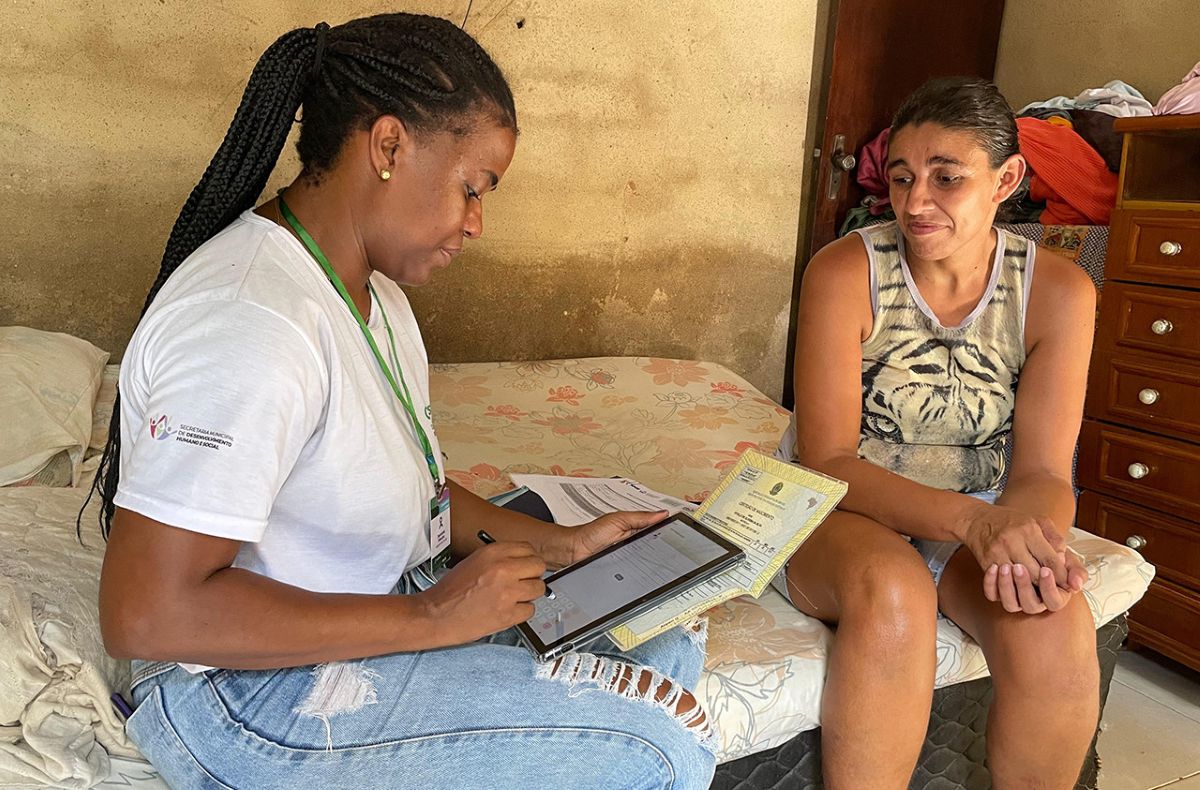 Agente social realiza visita domiciliar para atualizar cadastro de beneficiária em programa social.