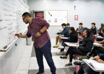 Professor explicando conteúdo na lousa em sala de aula, com alunos atentos