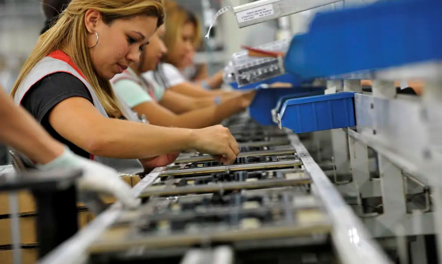 Mulher latina em linha de produção de eletrônicos, simbolizando a entrada de mães no trabalho formal após a ampliação do Bolsa Família 2025.