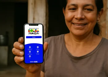 Mulher beneficiária sorri enquanto exibe o celular com o novo aplicativo "Programa Bolsa Família" na tela, destacando a seção de acesso e opções de consulta.