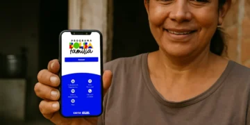Mulher beneficiária sorri enquanto exibe o celular com o novo aplicativo "Programa Bolsa Família" na tela, destacando a seção de acesso e opções de consulta.