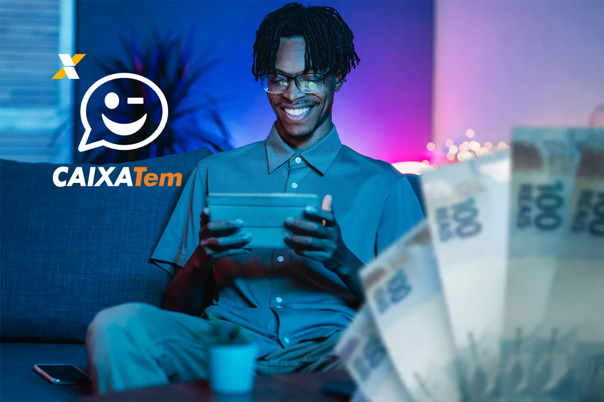 Um homem jovem e sorridente, com cabelo trançado, usando óculos, sentado em um sofá azul e olhando para um tablet.