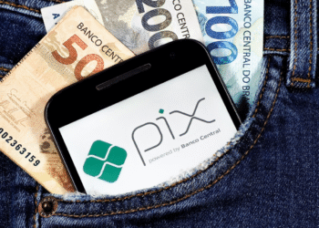Celular com logo do Pix e cédulas de real no bolso de uma calça jeans.