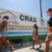 Pessoas, incluindo uma criança, caminhando em frente a um prédio com o letreiro 'CRAS - Centro de Referência de Assistência Social', indicando a busca por serviços sociais.