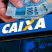 Imagem mostrando dinheiro sendo retirado de uma mão frente à fachada da Caixa Econômica Federal.