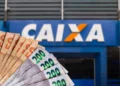 Cédulas de dinheiro reais em diversas quantias com a fachada da Caixa Econômica Federal desfocada ao fundo