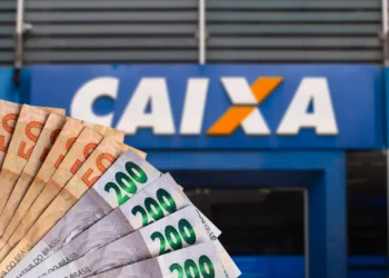 Cédulas de dinheiro reais em diversas quantias com a fachada da Caixa Econômica Federal desfocada ao fundo