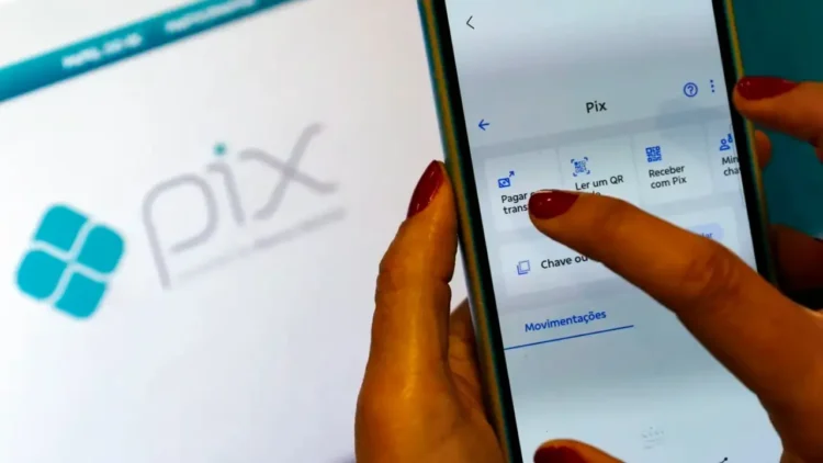 Mão feminina segurando um smartphone com a tela do aplicativo Pix aberta, mostrando opções de pagamento e leitura de QR Code, com a logo Pix ao fundo, ilustrando a função Pix por foto.