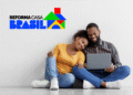 Casal sentado no chão sorrindo enquanto usa um notebook, ao lado do logotipo do programa Reforma Casa Brasil.