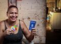 Mulher sorridente segura o cartão do Bolsa Família e uma Carteira de Trabalho, simbolizando a união do benefício social com a inserção profissional feminina.