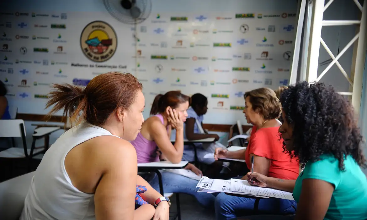 Pessoas em atendimento social em sala com carteira escolar e documentos na mão